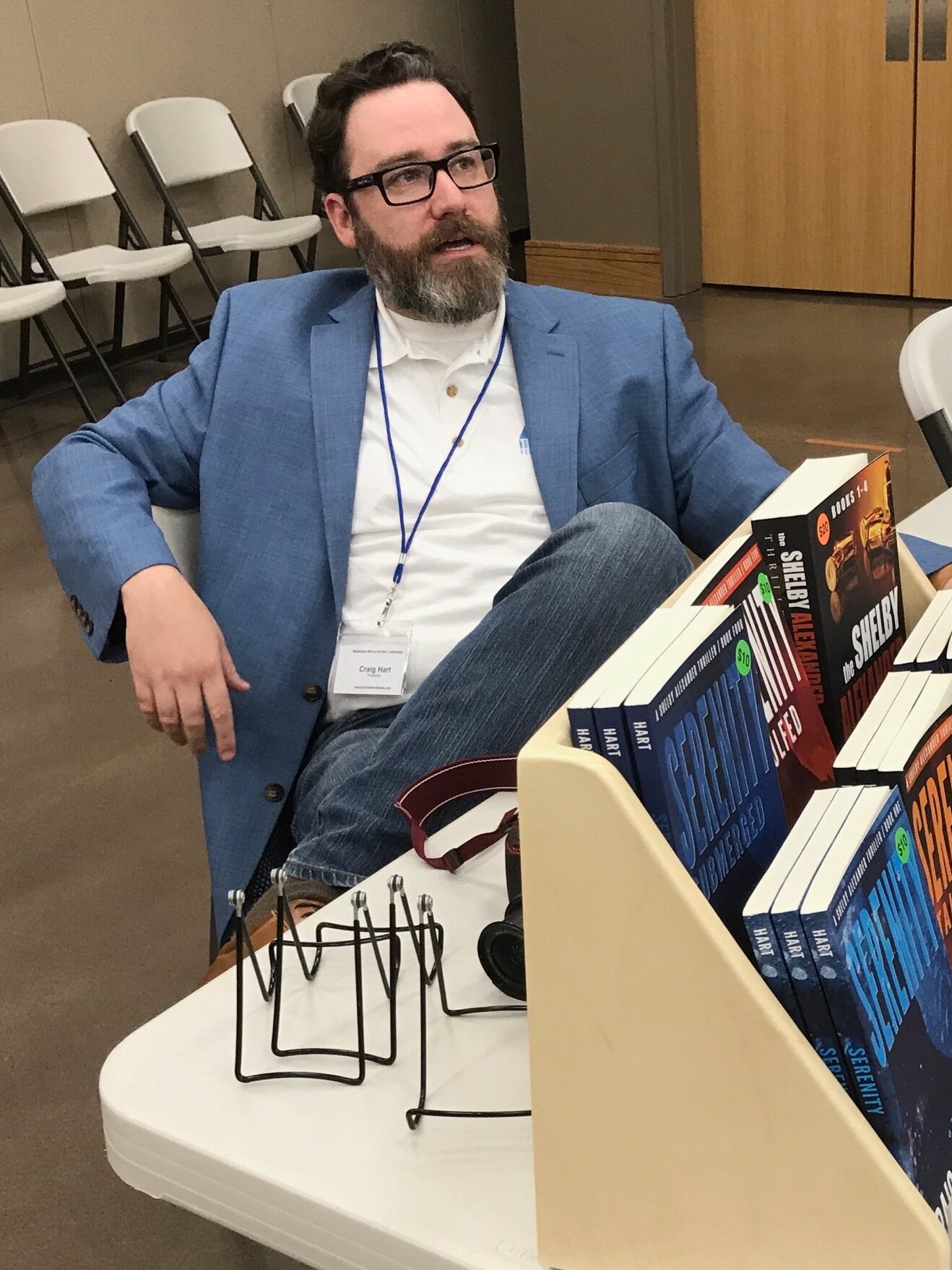 Craig A. Hart seated beside a display of Shelby Alexander books at an author event